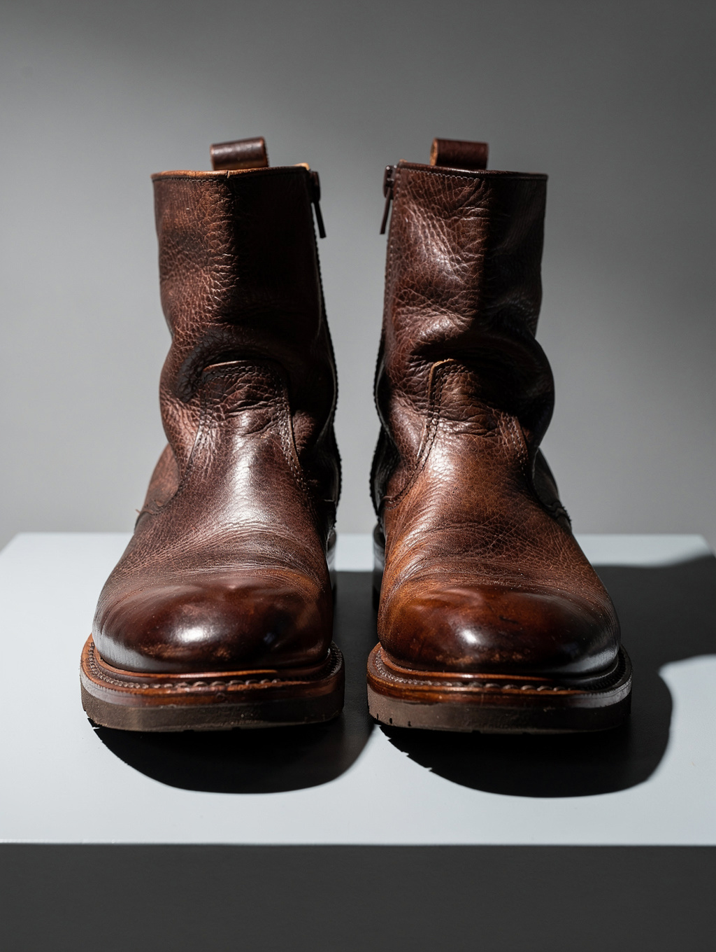 Low-angle profile photograph of handcrafted artisan boot rested upon a raw concrete pedestal